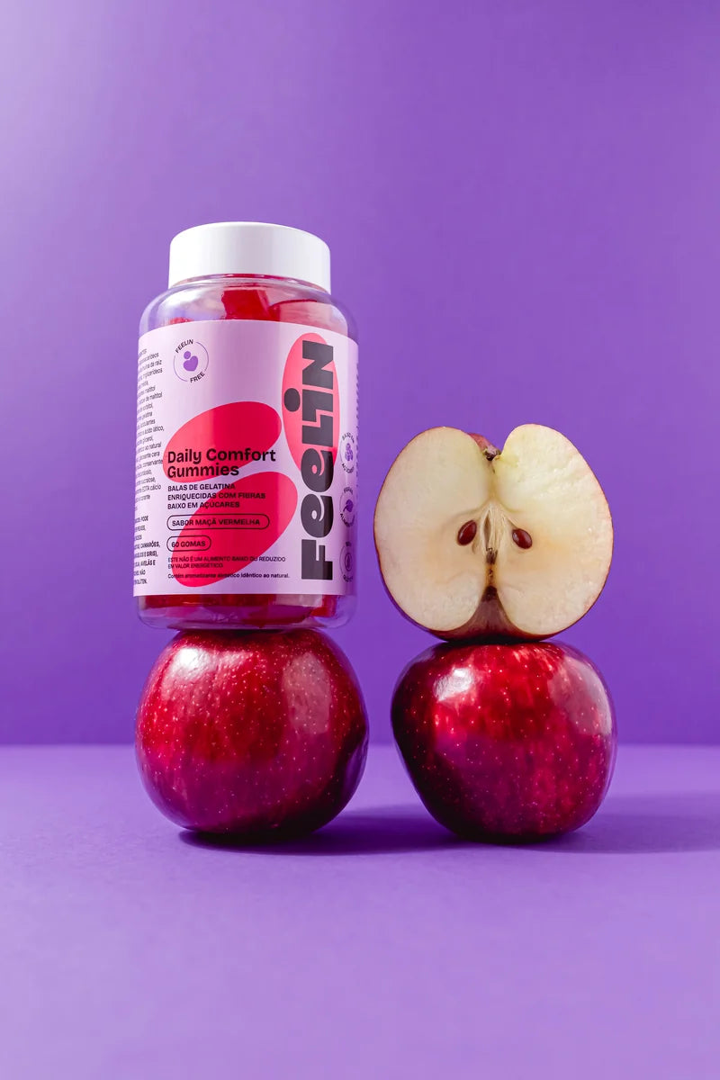 Dois potes de Feelin Gummies de Fibras Prebióticas ao lado de maçãs vermelhas, sobre fundo roxo.